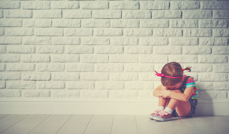 小女孩哭着伤心地看着砖墙。