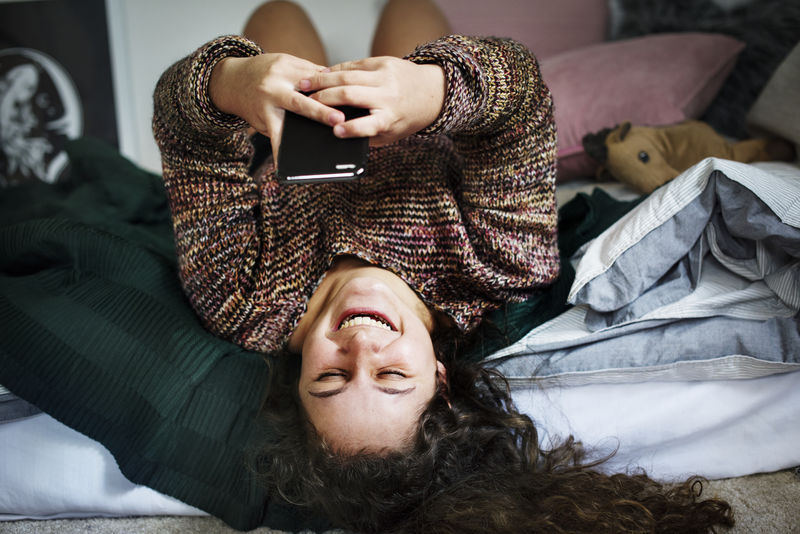 十几岁女孩在床上使用智能手机社交媒体和成瘾概念