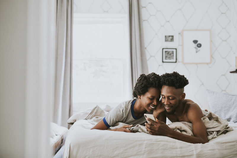 快乐的黑人夫妇在床上玩智能手机
