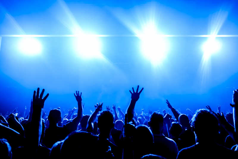 舞台灯光前音乐会台下举手欢呼的歌迷
