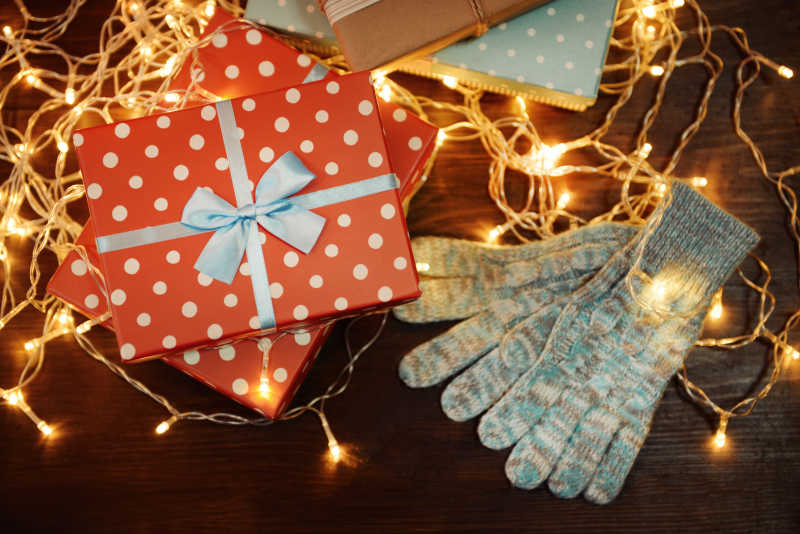 金色圣诞灯下漂亮的礼品盒和温暖的手套