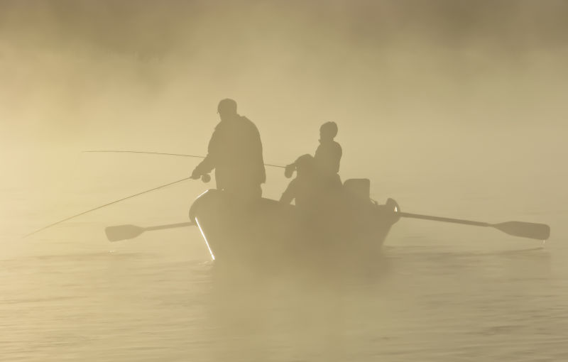 在迷雾中的小船上钓鱼的人