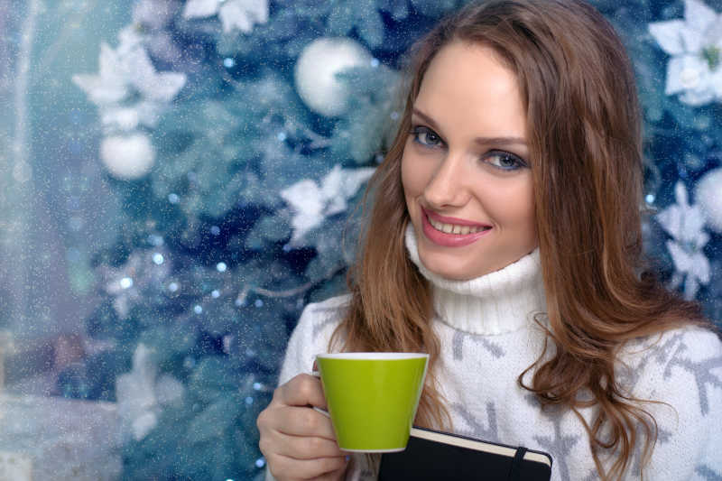 圣诞树前端着咖啡杯的年轻美女