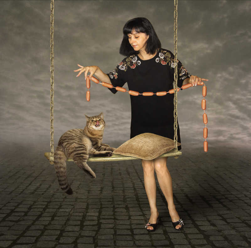 阴天背景下灰色地面上女人拿着一串香肠喂猫