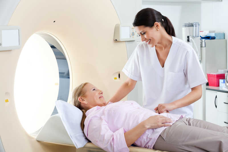 白色室内背景下躺在CT扫描床上的成熟女性患者和微笑技术员