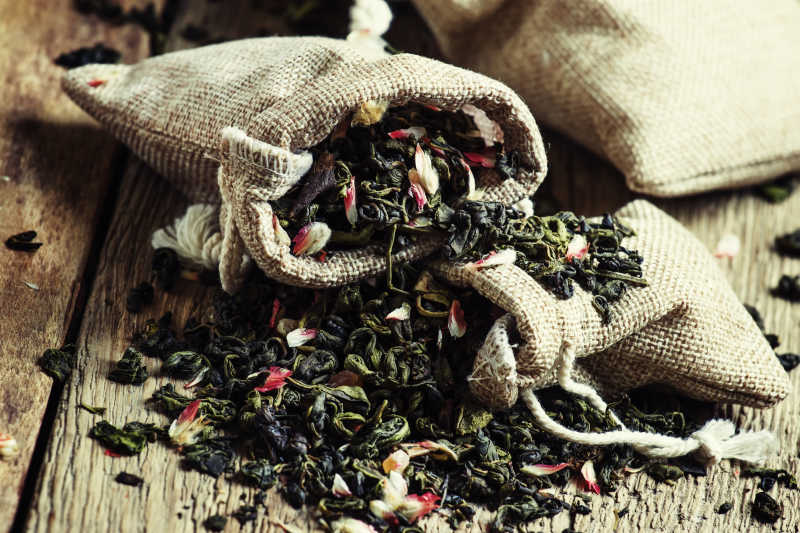 古董木卓背景中帆布袋散落的干花绿茶