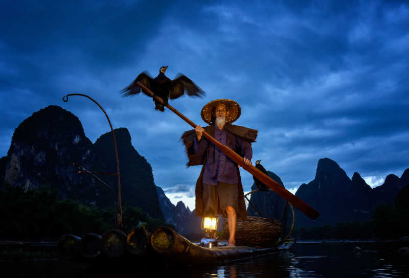 深夜的渔夫正划着竹筏在喂鸬鹚