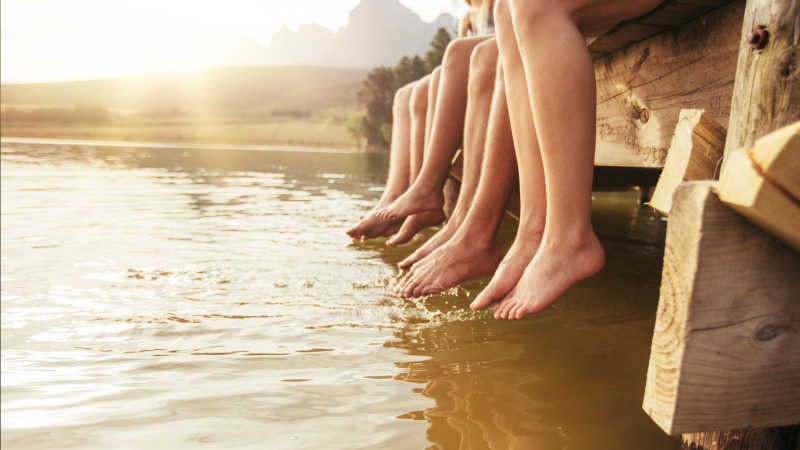 坐在湖边桥上双腿垂向水中的年轻人