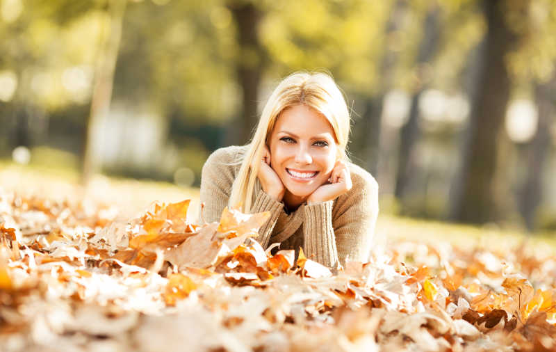 美丽的金发女人在树林中的落叶上微笑