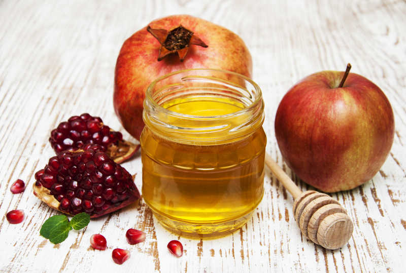 木桌面上的苹果石榴和罐装蜂蜜
