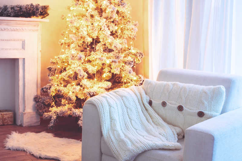 圣诞树装饰的房间有白色沙发和柔软的编织毯和垫子