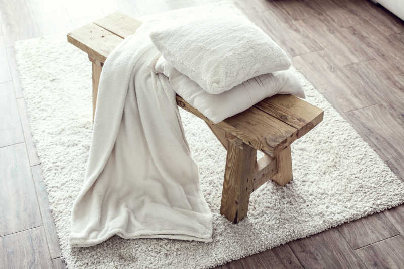 白色地毯上的长凳放着白色垫子和毯子