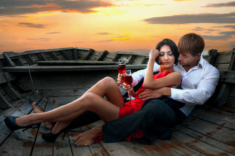 夕阳下老船上的浪漫夫妇喝红葡萄酒