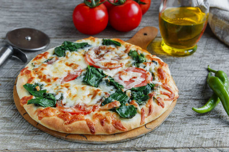木桌上自制的美味的菠菜西红柿芝士披萨