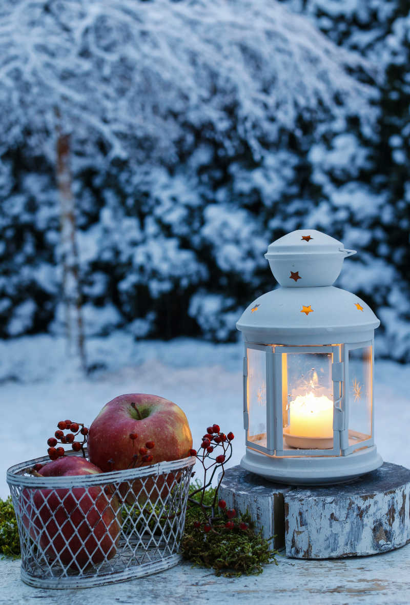 在花园里的冬天的夜晚的木桌上的铁灯笼和苹果篮子