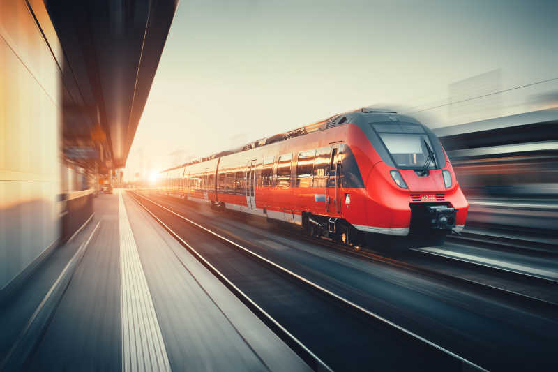 美丽的火车站与现代高速红色列车在模糊效果夕阳下行驶
