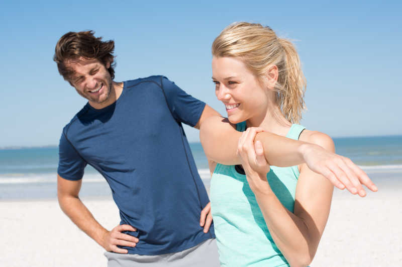 阳光灿烂的一对年轻夫妇在海滩上伸展身子