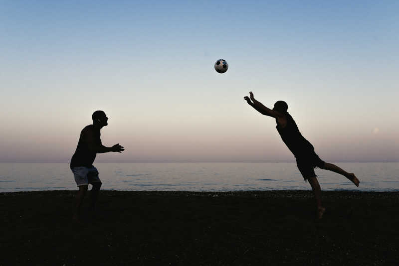 正在沙滩上踢足球的两个男人剪影