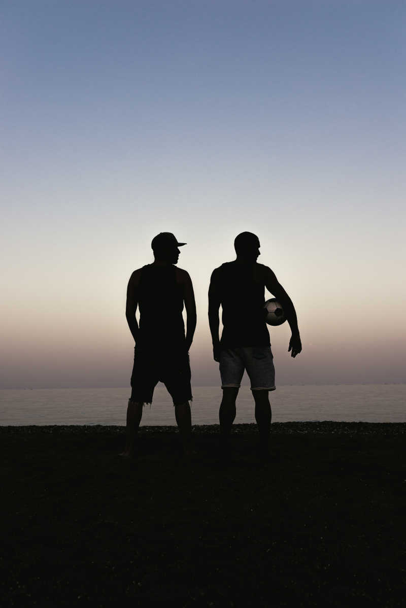 拿着足球站在沙滩上的两个男人剪影