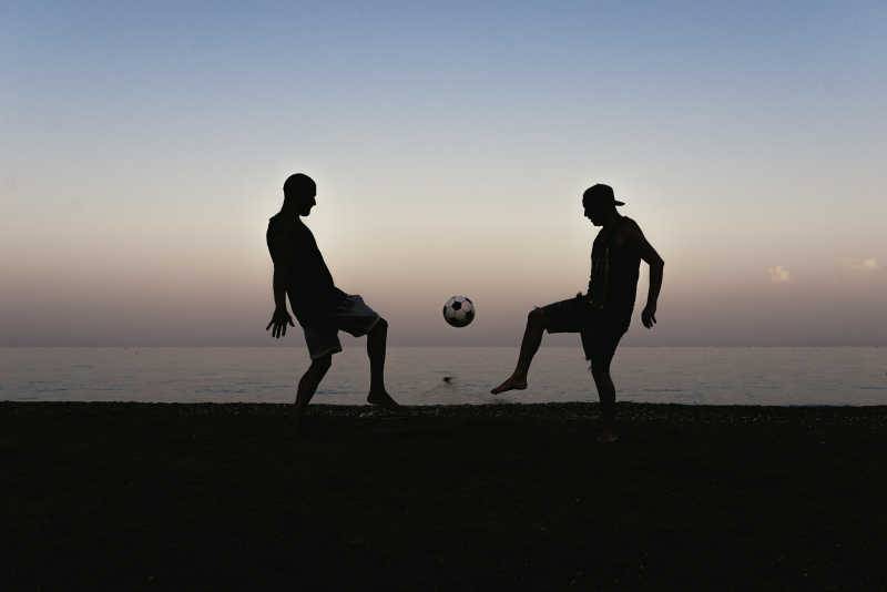 在沙滩上踢足球的两个男人剪影