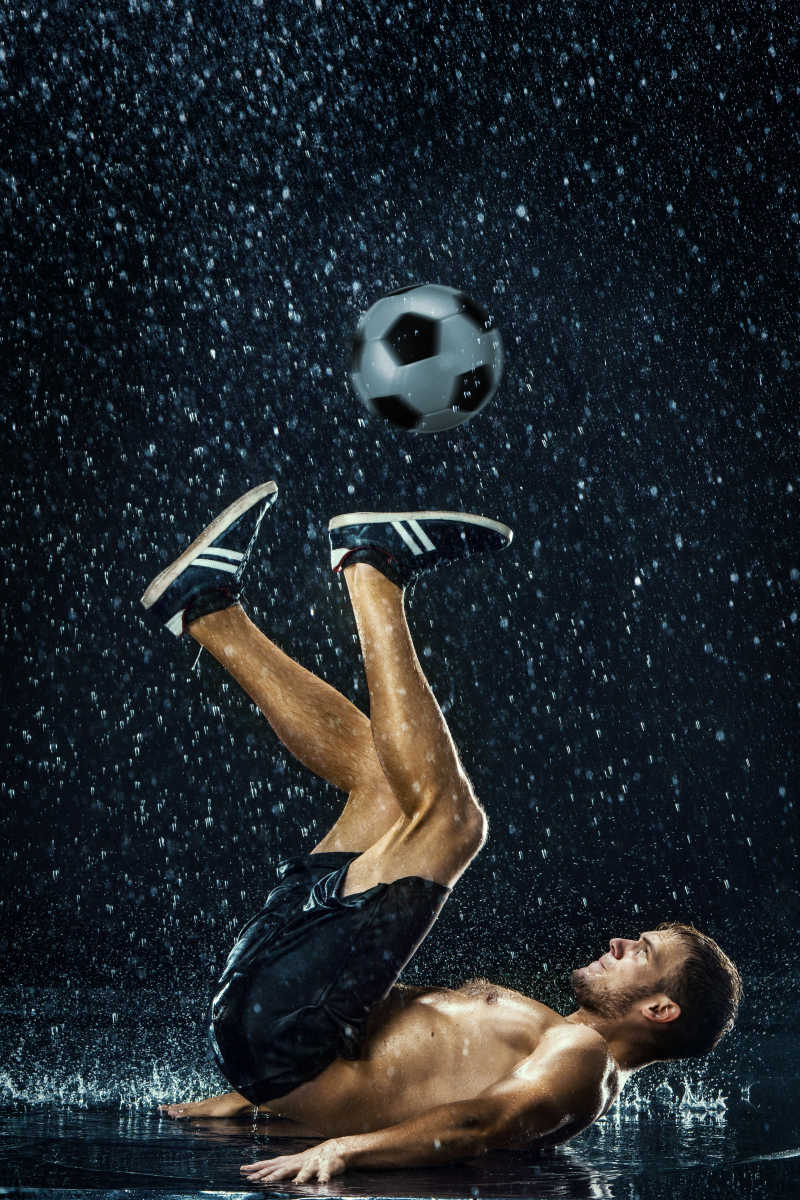 黑色背景下正在玩足球的足球运动员在水下的水滴