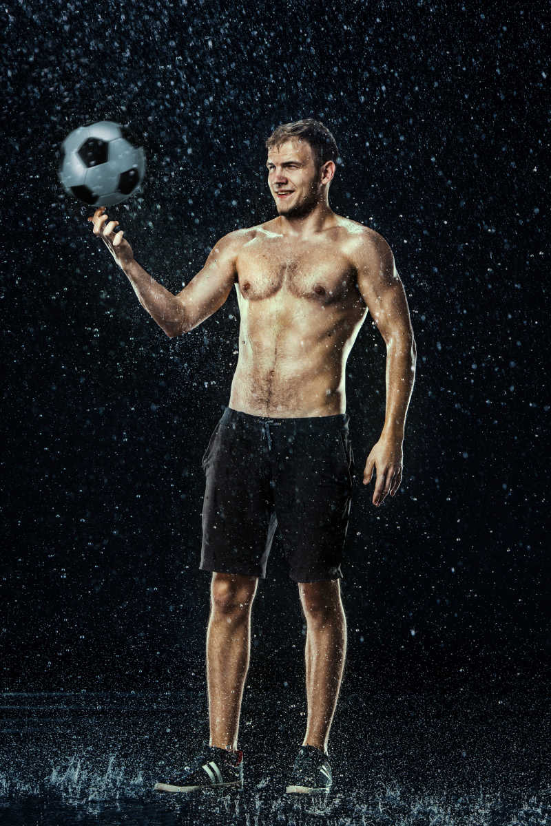 黑色背景下正在旋转足球的足球运动员在水下的水滴