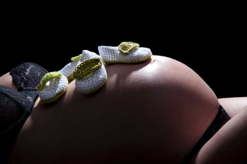 黑色背景下的孕妇腹部放置的婴儿鞋