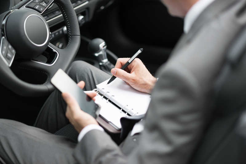 商人坐在车里使用智能手机和做笔记