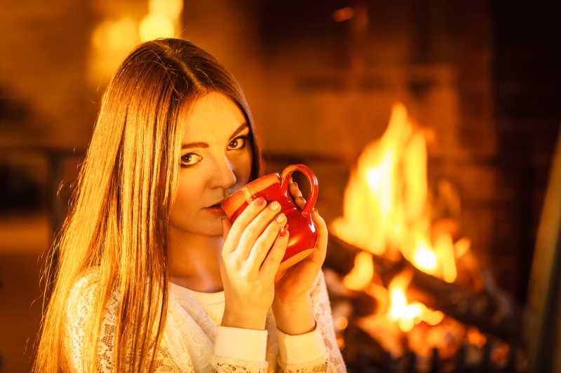 在燃烧壁炉旁喝着热咖啡的女孩