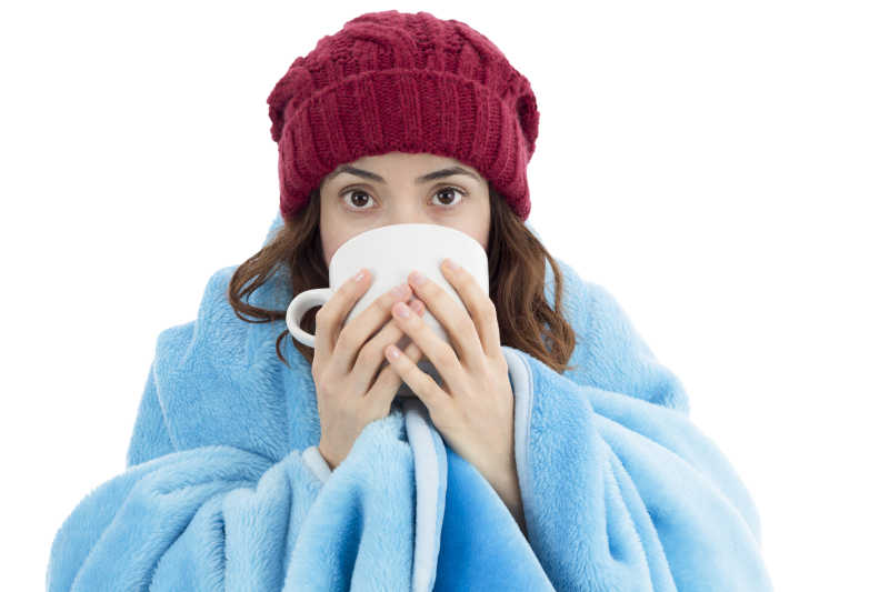 白色背景下寒冷的女人包裹着毯子喝茶