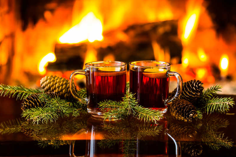 两杯红酒或热饮茶配圣诞装饰冷杉枝条在暖壁炉前
