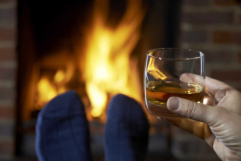 喝杯威士忌放松的人和燃烧的室内壁炉