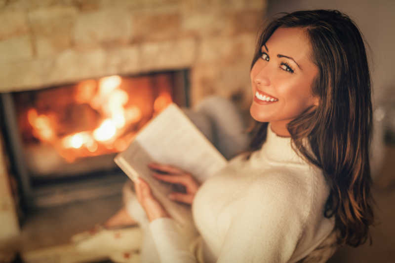 美丽的年轻女人在读书壁炉边享受