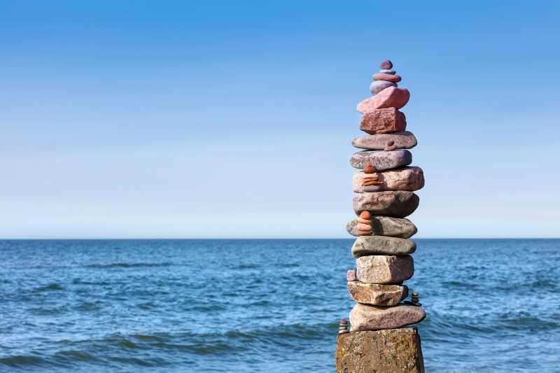 蓝天下还水边堆叠的石头的平衡与和谐的概念