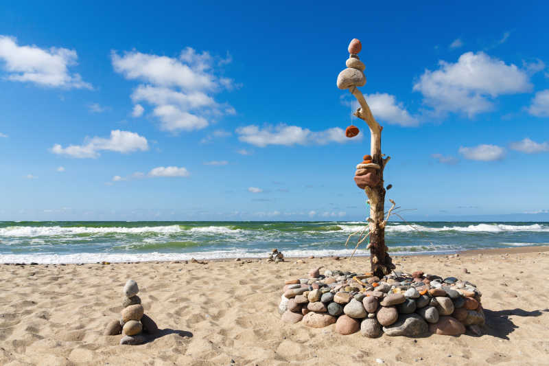 蓝天白云背景下海边沙滩上堆叠的石头的平衡与和谐的概念