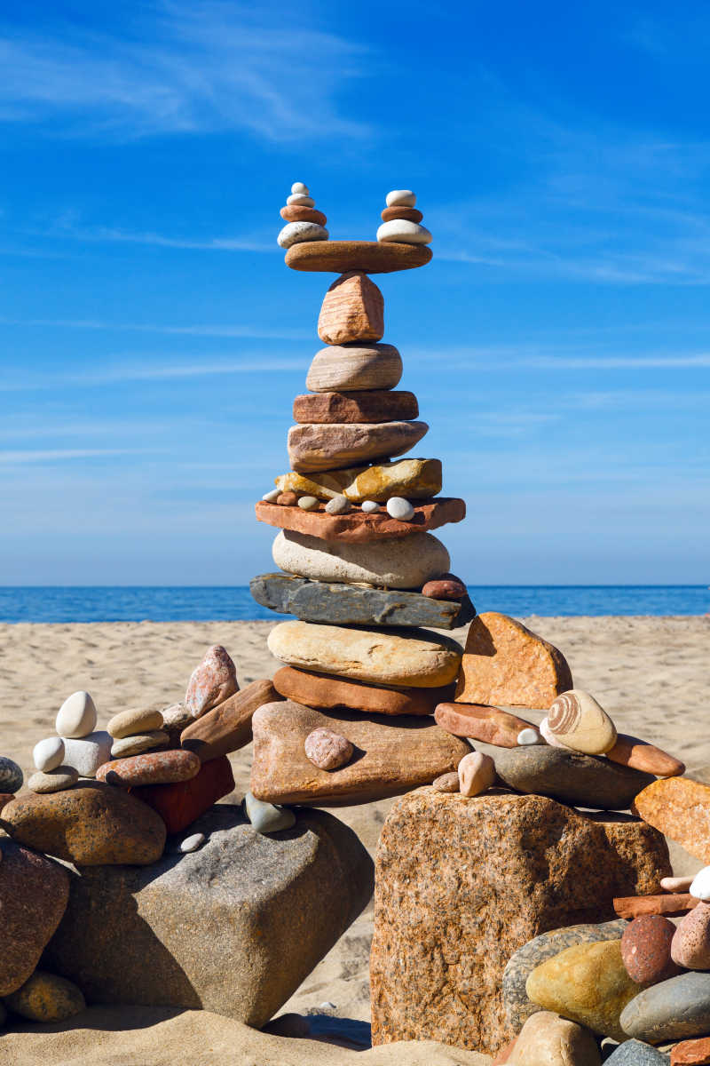 蓝天下黄色沙滩上堆叠的石头的平衡与和谐的概念