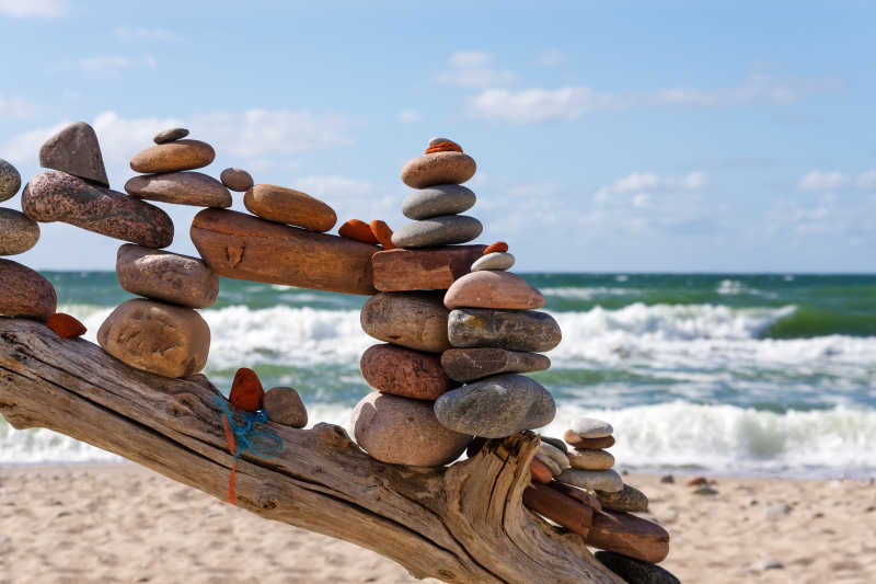 蓝天白云背景下海边沙滩上树干上堆叠的石头的平衡与和谐的概念