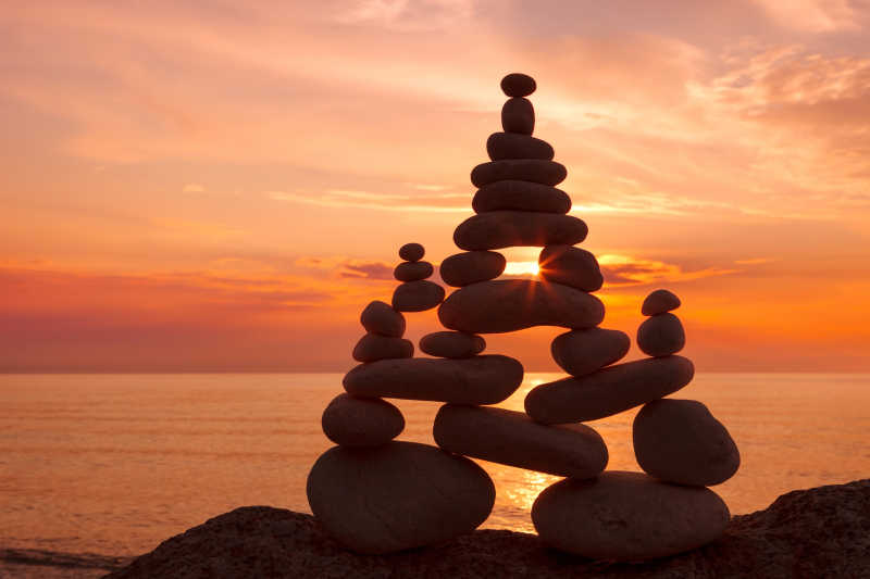 日落时分海边沙滩上的堆叠的石头的平衡与和谐的概念