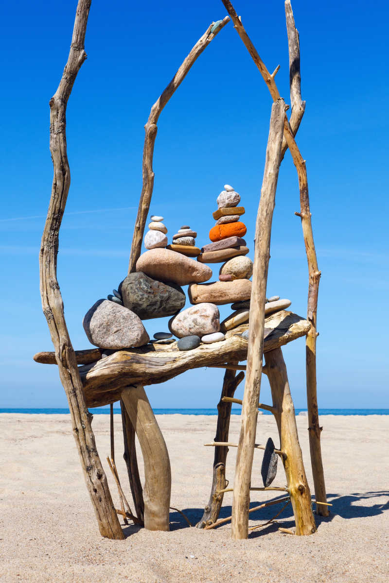 蓝天下沙滩上堆叠的石头和树干的和谐与平衡的概念