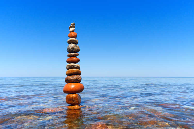 蓝色天空下海水里堆叠的石头的和谐与平衡的概念