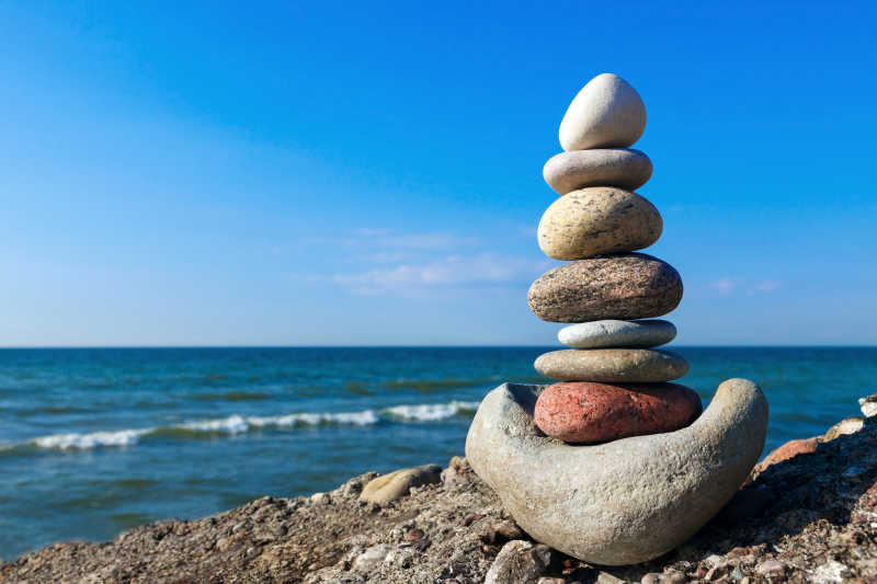 蓝色海边沙滩上堆叠的石头的和谐与平衡的概念