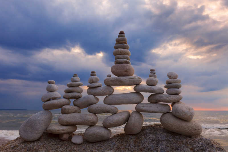 有云的天空下海边堆叠的石头的和谐与平衡的概念