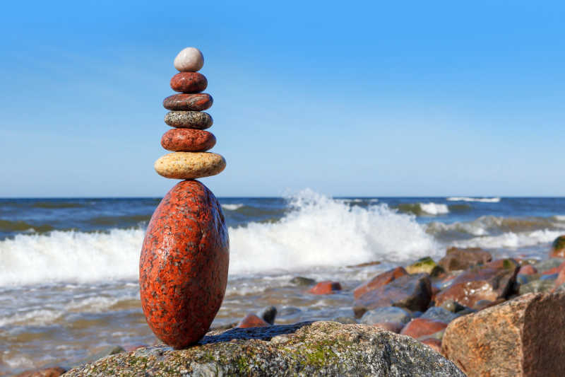 蓝色天空下海边浅滩上堆叠的石头的和谐与平衡的概念