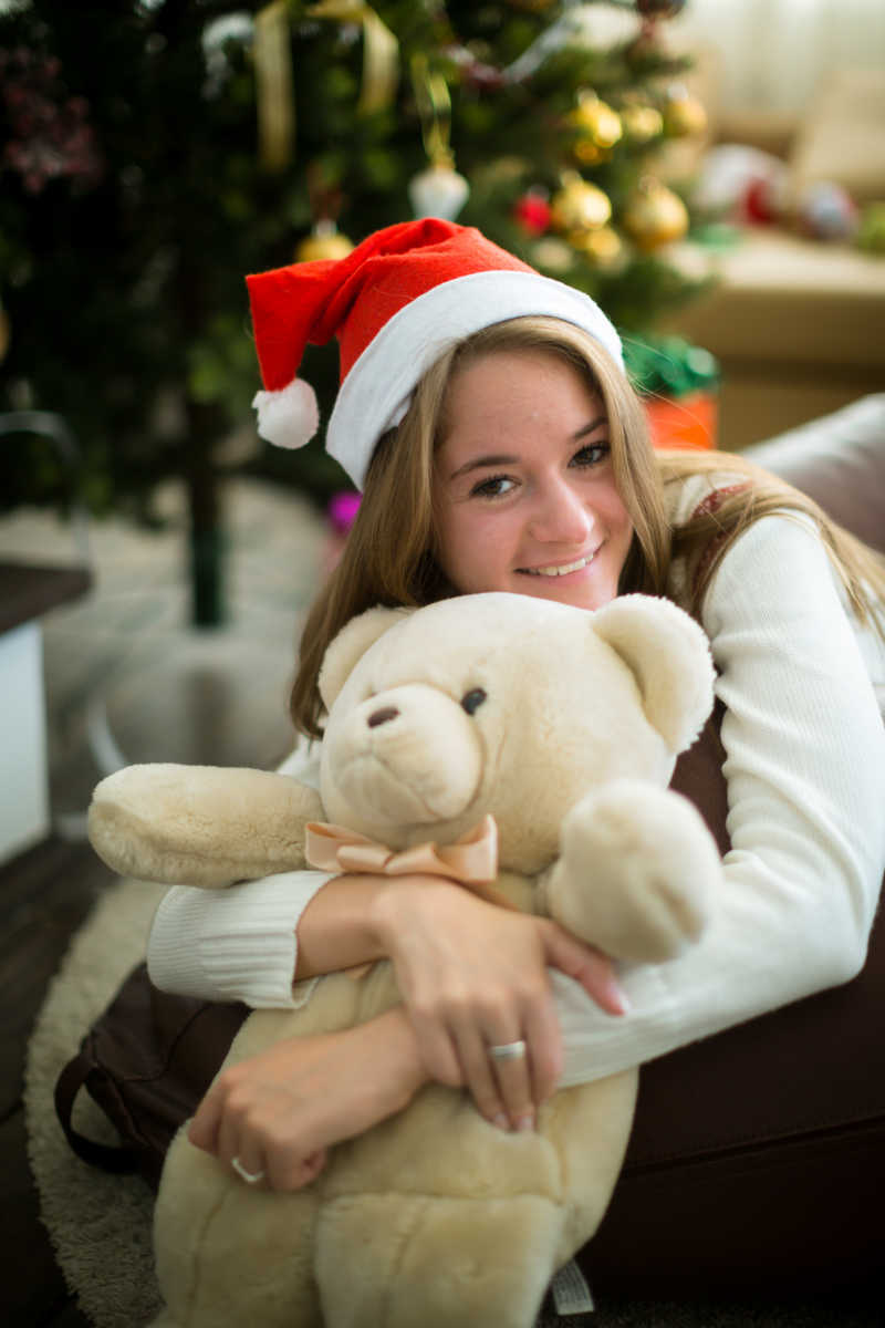 圣诞树旁抱着泰迪熊的女孩