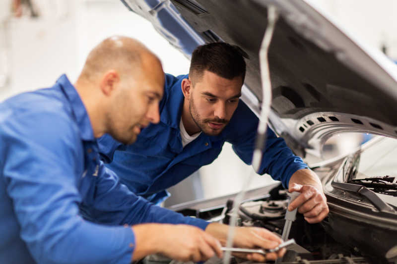 两名男性汽车修理工合作维修汽车