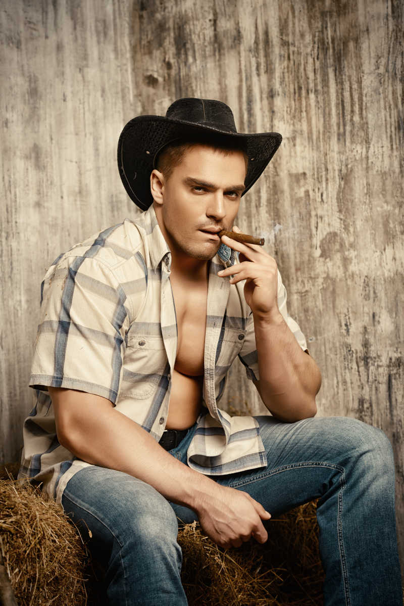 坐在草堆上抽着雪茄的时尚男性模特