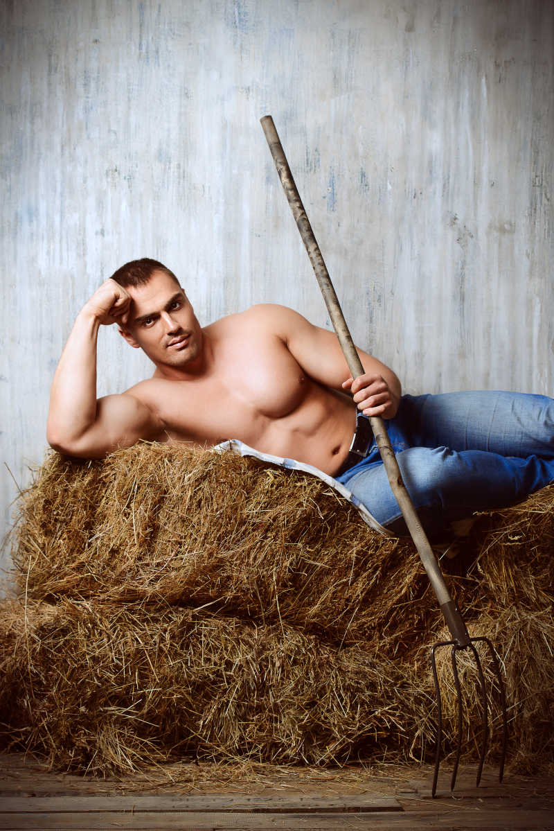 半裸的躺在草堆上手拿工具的时尚男性模特