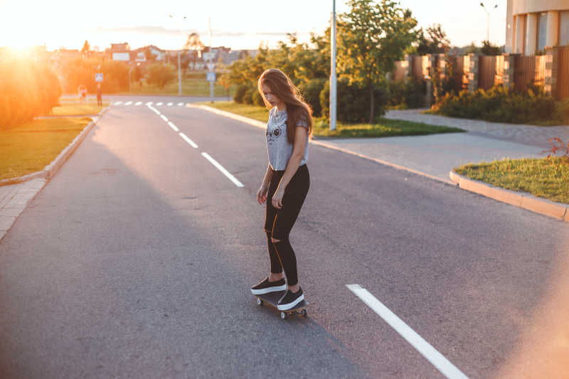 夕阳下在马路上玩滑板的年轻女孩
