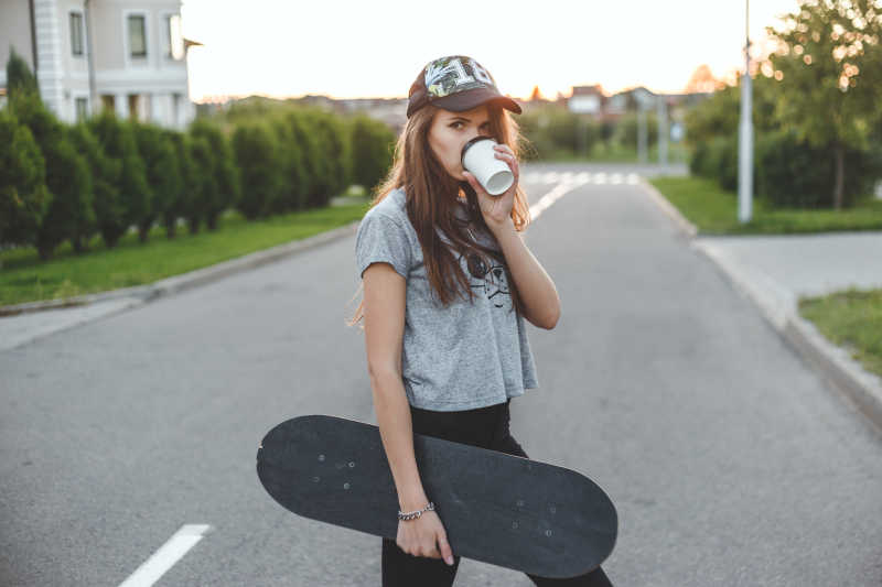 马路上拿着滑板喝咖啡的时尚女孩