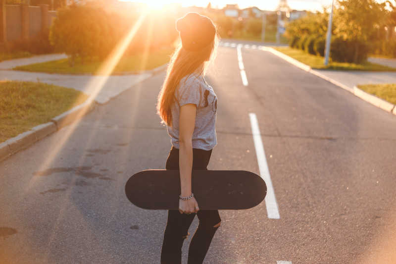 阳光下拿着滑板的年轻女孩